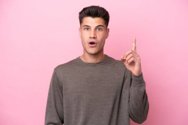 Pembe arka planda izole edilmiş genç beyaz bir adam bir fikri işaret ederek...