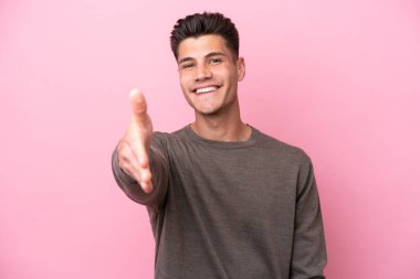Pembe arka planda izole edilmiş genç beyaz adam iyi bir anlaşma için el sıkışıyor.