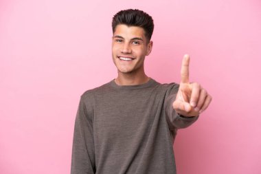 Pembe arka planda izole edilmiş genç beyaz adam parmağını kaldırıyor ve gösteriyor.