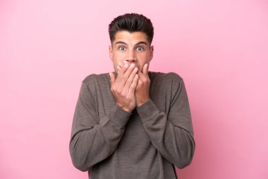 Pembe arka planda izole edilmiş genç beyaz adam elleriyle ağzını kapatıyor.