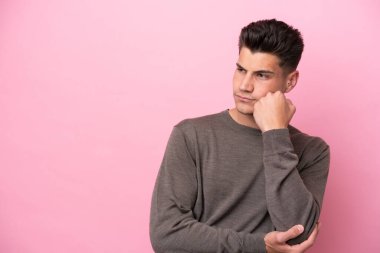 Pembe arka planda soyutlanmış, yorgun ve sıkılmış bir ifadeyle genç beyaz bir adam.
