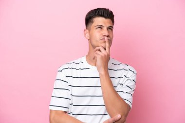 Pembe arka planda izole edilmiş genç beyaz adam yukarı bakarken şüphe duyuyor.