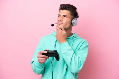 Pembe arka planda izole edilmiş bir bilgisayar oyunu kontrolörüyle oynayan yakışıklı beyaz bir adam.