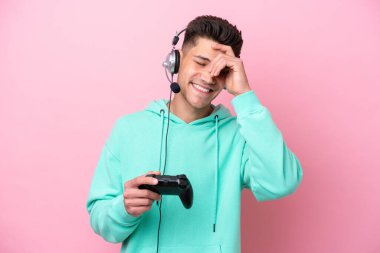 Pembe arka planda izole edilmiş bir bilgisayar oyunu kontrolörüyle oynayan yakışıklı beyaz adam gülüyor.