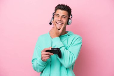 Pembe arka planda izole edilmiş bir bilgisayar oyunu kontrolörüyle oynayan yakışıklı beyaz adam mutlu ve gülümsüyor.