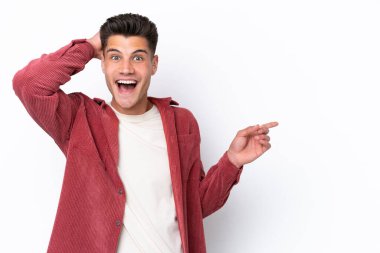 Beyaz arka planda izole edilmiş genç, beyaz bir adam şaşırmış ve parmağıyla kenarı işaret ediyor.