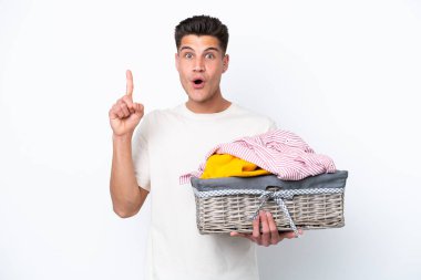 Beyaz arka planda çamaşır sepetini tutan beyaz tenli genç adam çözümü bulmak için parmağını kaldırıyor.