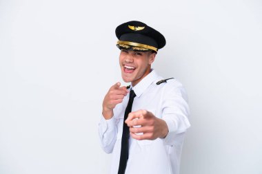 Kafkasyalı uçak pilotu beyaz arka planda izole edilmiş ön tarafı işaret ediyor ve gülümsüyor.