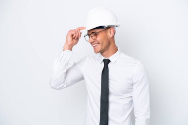 Beyaz arka planda izole edilmiş miğferli ve elinde planları olan genç bir beyaz adam gülüyor.