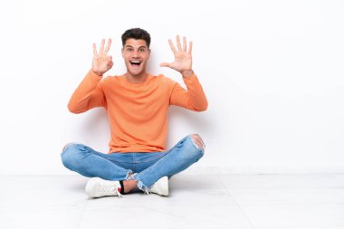 Yerde oturan genç adam beyaz arka planda izole edilmiş, parmaklarıyla sekiz kişi sayıyor.