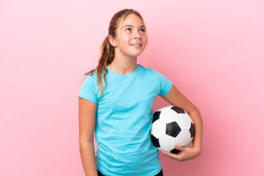 Little football player girl isolated on pink background thinking an idea while looking up