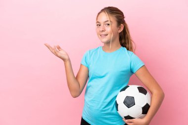 Pembe arka planda izole edilmiş küçük futbolcu kız, davet edilmek için ellerini yana uzatıyor.
