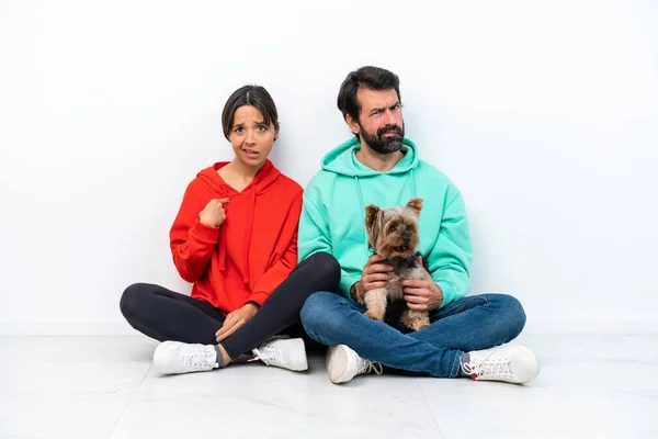 Young caucasian couple sitting on the floor with their pet isolated on white background annoyed angry in furious gesture