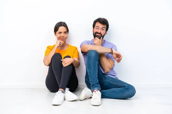 Young Caucasian Couple Sitting Floor Isolated White Background Having Doubts — Stock fotografie