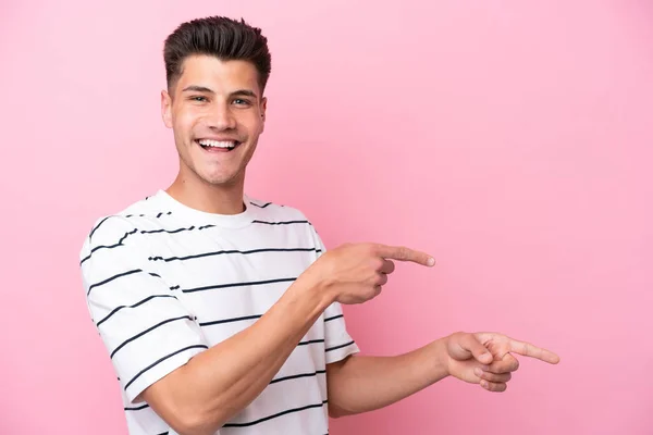 ピンクの背景の指を横に向けて製品を提示する若い白人男性 — ストック写真