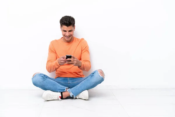 Mladý Muž Sedí Podlaze Izolovaný Bílém Pozadí Posílá Zprávu Mobilem — Stock fotografie