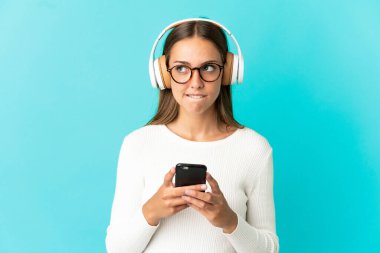 İzole edilmiş mavi arka planda genç bir kadın cep telefonu ve düşünce gücüyle müzik dinliyor.