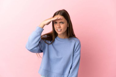 Soyutlanmış pembe arka planı olan genç bir kadın bir şeye bakmak için çok uzaklara bakıyor.