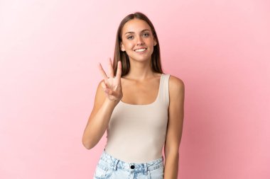 Genç bir kadın pembe arka planda mutlu ve parmaklarıyla üçe kadar sayıyor.