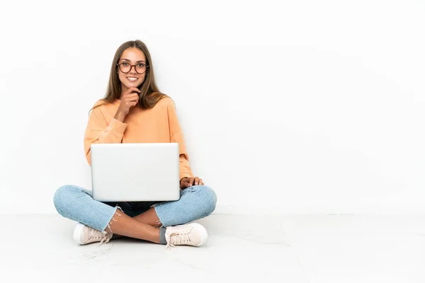 拿着笔记本电脑的年轻女人坐在地板上 戴着眼镜 面带微笑 — 图库照片