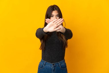 Sarı arka planda izole edilmiş Brezilyalı genç bir kız, bir hareketi durdurmak için elleriyle dur hareketi yapıyor.