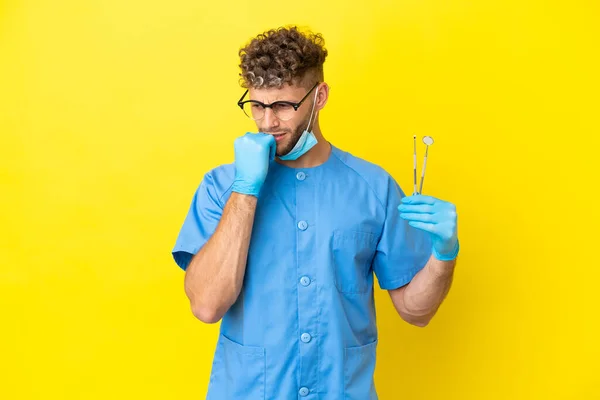Zubař Blondýny Muž Drží Nástroje Izolované Pozadí Pochybnostmi — Stock fotografie