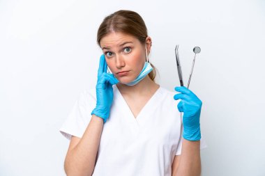 Beyaz arka planda izole edilmiş aletleri tutan beyaz dişçi kadın bir fikir düşünüyor.