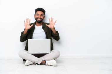 Yerde dizüstü bilgisayarı olan genç Brezilyalı bir adam, beyazı izole edip parmaklarıyla 10 'u sayıyor.