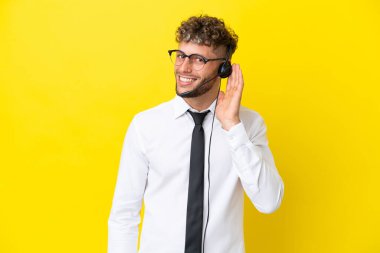 Sarı arka planda izole edilmiş bir kulaklıkla çalışan pazarlamacı sarışın adam bir şey dinlerken elini kulağına koydu.