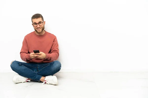 年轻英俊的男子坐在地板上 用手机传递信息 — 图库照片