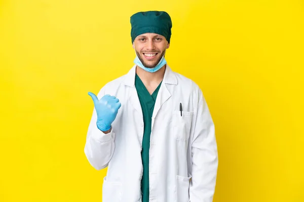 Χειρούργος Ξανθός Άνδρας Πράσινη Στολή Απομονώνεται Κίτρινο Φόντο Που Δείχνει — Φωτογραφία Αρχείου