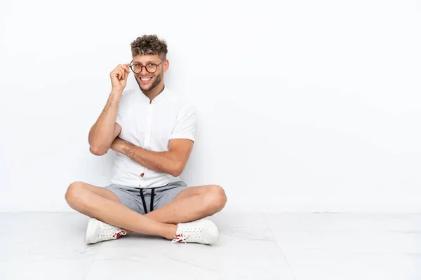 Young Blonde Man Sitting Floor Isolated White Background Glasses Happy — Stockfoto