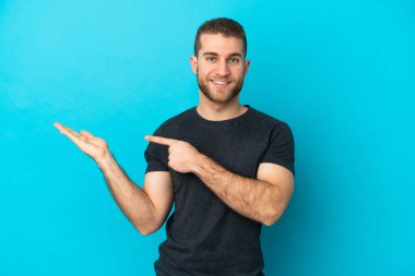 Mavi arka planda izole edilmiş yakışıklı beyaz adam bir ilan vermek için fotokopi makinesini avucunun içinde tutuyor.