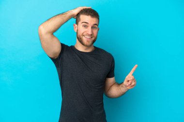 Mavi arka planda izole edilmiş yakışıklı beyaz adam şaşırdı ve parmağını yana çevirdi.
