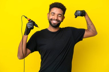 Dövmeli adam Brezilyalı izole edilmiş sarı arka planda güçlü bir jest yapıyor.