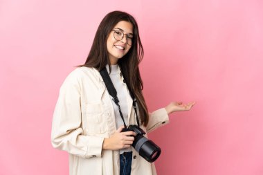 Genç fotoğrafçı Brezilyalı kız pembe arka planda izole edilmiş, davet edildiği için ellerini yana uzatıyor.
