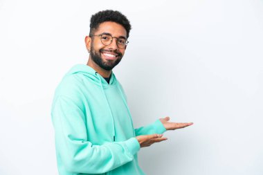 Beyaz arka planda izole edilmiş genç Brezilyalı adam, davet etmek için ellerini yana uzatıyor.