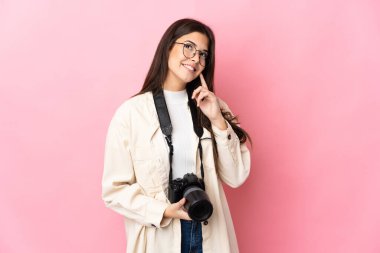 Genç fotoğrafçı Brezilyalı kız pembe arka planda izole edilmiş bir şekilde yukarı bakarken bir fikir düşünüyor.