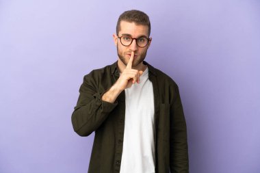 Mor arka planda izole edilmiş yakışıklı beyaz adam sessiz bir jest işareti gösteriyor. Parmağını ağzına sokuyor.