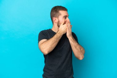 Genç beyaz adam mavi arka planda izole edilmiş ağzını kapatıyor ve yan tarafa bakıyor.