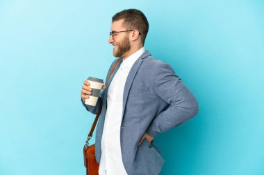 Kafkasyalı genç işadamı mavi arka planda izole edilmiş, gayret gösterdiği için sırt ağrısı çekiyor.