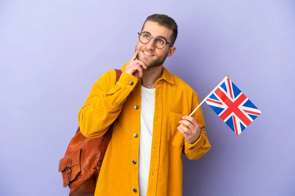 Młody Biały Mężczyzna Trzymając Flagę Wielkiej Brytanii Odizolowany Fioletowym Tle — Zdjęcie stockowe