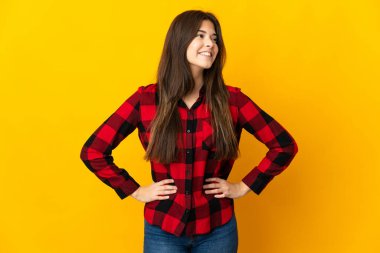 Sarı arka planda izole edilmiş genç Brezilyalı kız kolları kalçasında ve gülümsüyor.