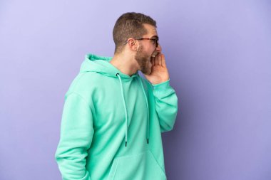 Mor arka planda izole edilmiş yakışıklı beyaz adam ağzı sonuna kadar açık bağırıyor.