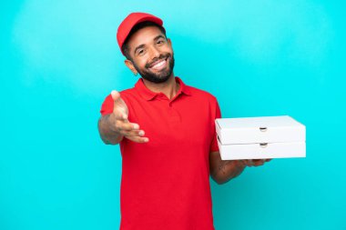 İş üniformalı bir Brezilyalı, mavi arka planda izole edilmiş pizza kutularını topluyor ve iyi bir anlaşma için el sıkışıyor.