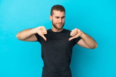 Mavi arka planda soyutlanmış, iki eliyle baş parmağını gösteren yakışıklı beyaz bir adam.