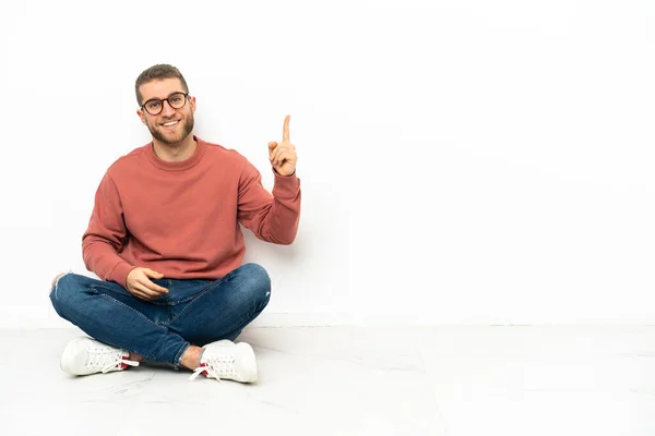 Mladý Pohledný Muž Sedí Podlaze Ukazuje Zvedá Prst Znamení Toho — Stock fotografie