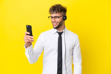 Sarı arka planda izole edilmiş kulaklıkla çalışan sarışın bir pazarlamacı selfie çekiyor.