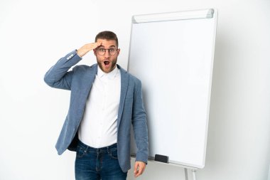 Beyaz arka planda izole edilmiş yakışıklı beyaz adam beyaz tahtada sunum yapıyor ve sürpriz bir ifadeyle