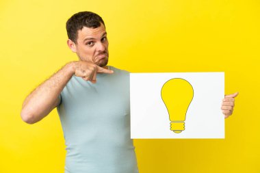 İzole edilmiş mor arka plan üzerinde Brezilyalı bir adam elinde ampul simgesi olan bir levha tutuyor ve ona doğrultuyor.